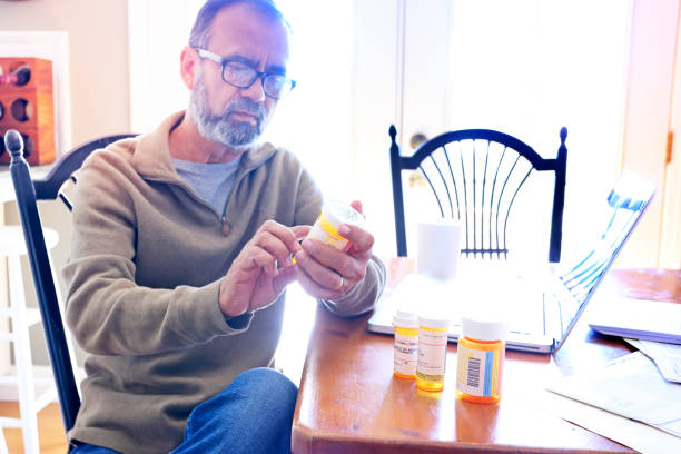 istock Hispanic Man Sitting At Dining Room Table Looking At His Prescription Medications 990720678