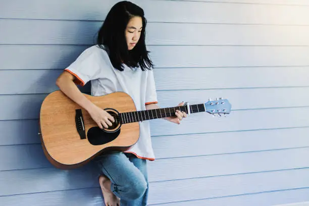 Photo of Asian girl enjoy practice guitar at home