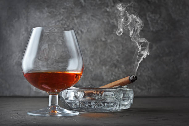 istock Strong alcoholic drink cognac in sniffer glass with smoking cigar in crystal ashtray 990821914