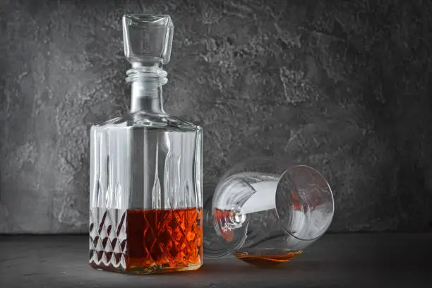 Strong alcoholic drink cognac in lying sniffer glass and crystal decanter on gray concrete background