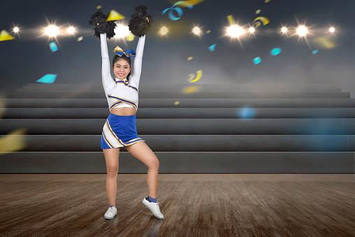 Attractive asian cheerleader with pom poms at indoor arena