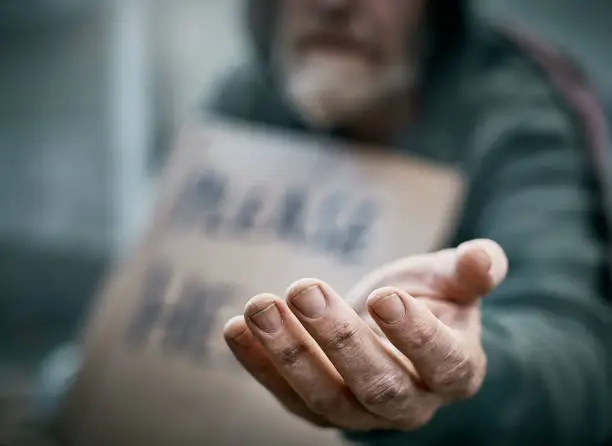 A pathetic homeless man begs on the sidewalk.