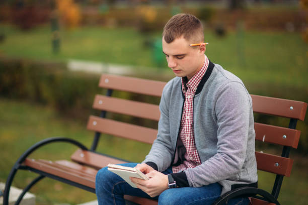 istock A cute student sits on the bench writes down his thoughts in his notebool using a pensil 990905882