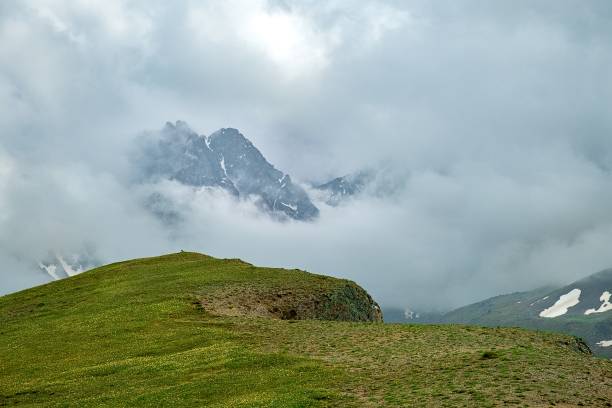 istock mountain plateau covered with green grass and a mountain peak surrounded by dense clouds 990907058