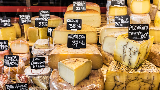 A large selection of different french and italian cheeses on the counter of a small store at the market in the Bastille district. Paris, France