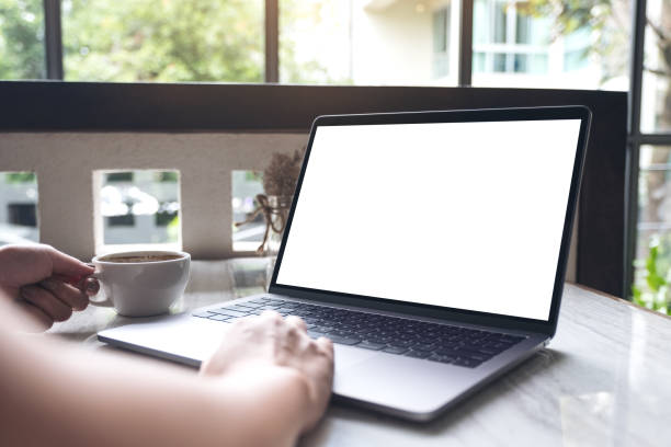 istock Mockup image of a woman using and typing on laptop with blank white screen while drinking coffee in modern cafe 990918012