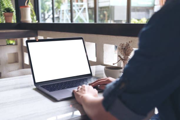 istock Mockup image of a woman using and typing on laptop with blank white screen and coffee cup on table in modern cafe 990918130