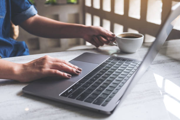 istock Closeup image of a woman working and typing on laptop keyboard while drinking coffee in office 990918134
