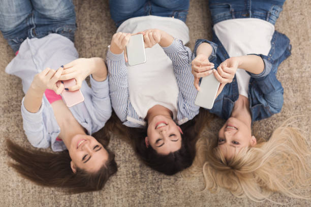 istock Happy girls lying on floor and using smartphones, top view 990919208