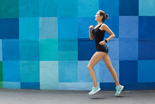 Side view of female athlete running against bright colorful graffiti wall, copy space