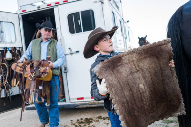 giovane cowboy prende virare dal rimorchio del cavallo per appiattire il padre porta la sella per lui - teaching child horseback riding horse foto e immagini stock