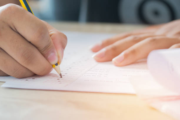istock Education test concept : Man Hands high school, university student holding pencil for testing exams writing answer sheet and exercise for taking in exam paper on wood table at classroom with uniform 990946620