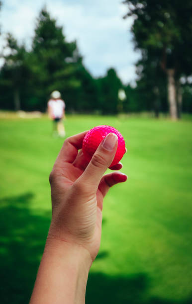 гольф розовый мяч держать в руке женщины, зеленая трава конечно, голубое небо. - golf women pink ball стоковые фото и изображения