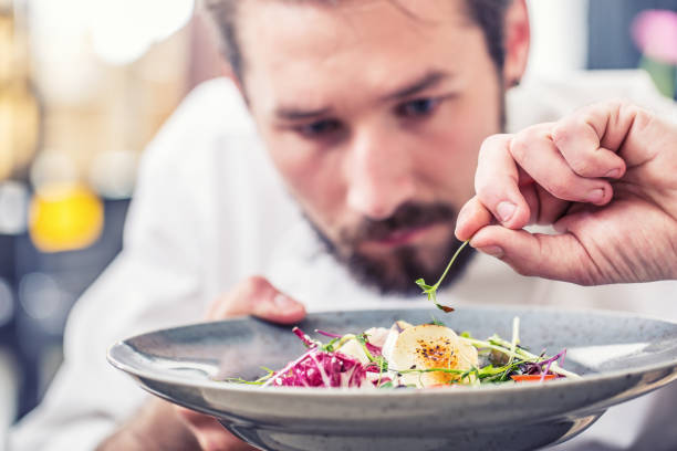 istock Chef in hotel or restaurant kitchen preparing meal vegetable salad with goat cheese and decorates the food with her hands 991036118