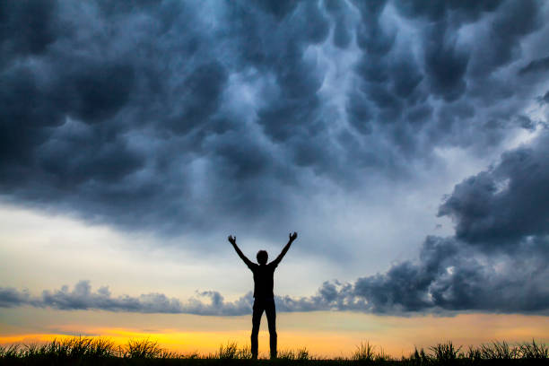 istock A young man alone holding his hands up against a dramatic sky at dusk. 991041598