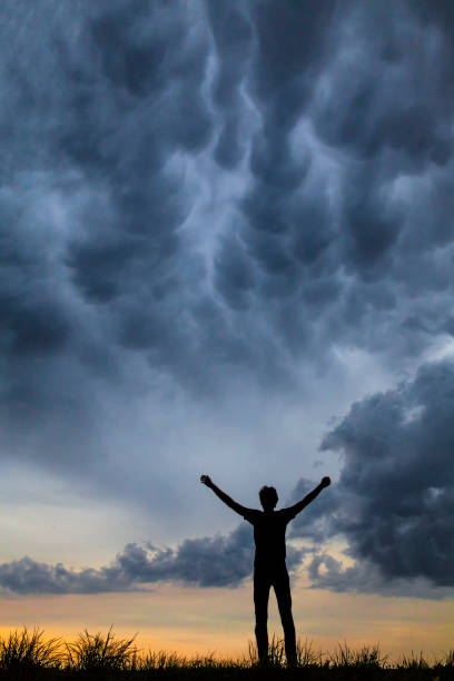 istock A young man alone holding his hands up against a dramatic sky at dusk. 991041668