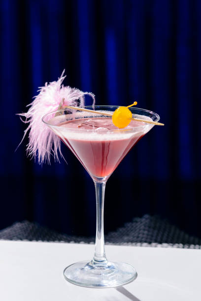 istock Alcoholic pink cocktail in a martini glass with straw on blue ba 991042716