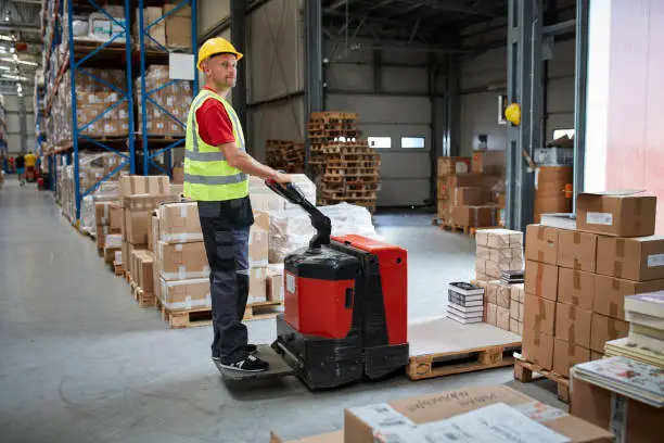 Male worker distributing cardboard boxes in a warehouse