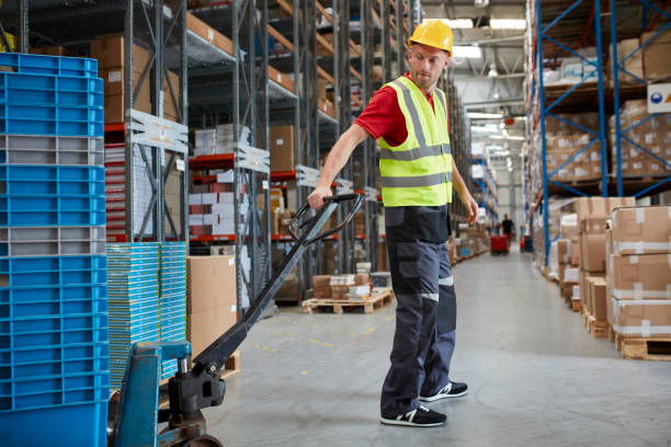istock Warehouse worker walking among shelves with handcart 991053354