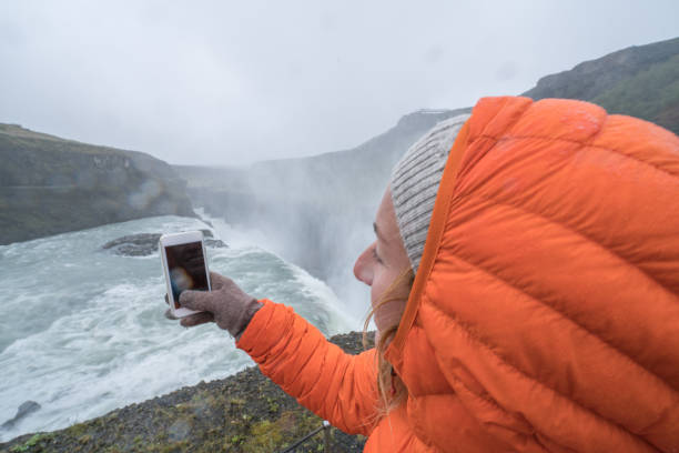 istock Young woman taking mobile phone picture at waterfall 991143350