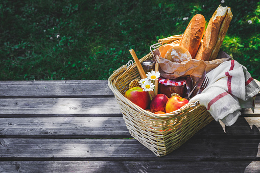 Picnic basket filled with fruit , bread and jar with apricot jam on wooden table.