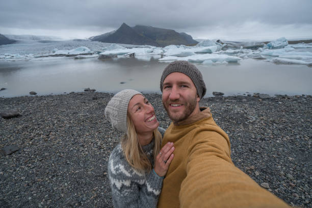 istock Young couple taking selfie with glacier lagoon, icebergs floating on water 991165138