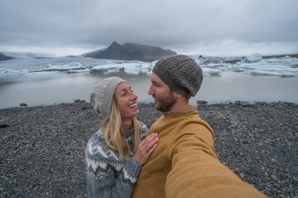 istock Young couple taking selfie with glacier lagoon, icebergs floating on water 991165154