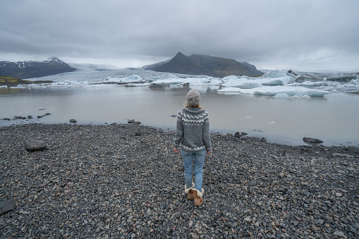Young woman contemplating glacier lake with icebergs floating. People travel exploration and climate change concept