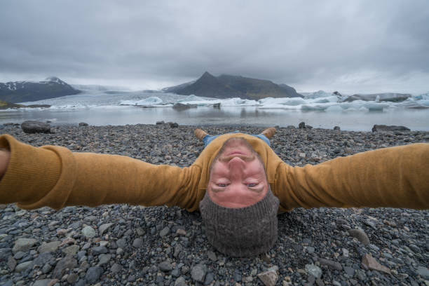 istock Young man taking upside down selfie with glacier lake, icebergs floating on water 991167152