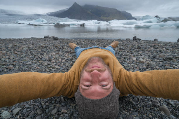 istock Young man taking upside down selfie with glacier lake, icebergs floating on water 991167154