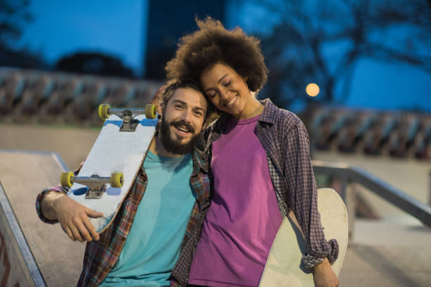 istock Happy woman with closed eyes hugging a man with skateboard 991167174