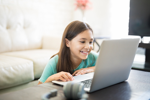 Cute latin girl smiling and sitting at home using a laptop computer to do her class work and browse the internet