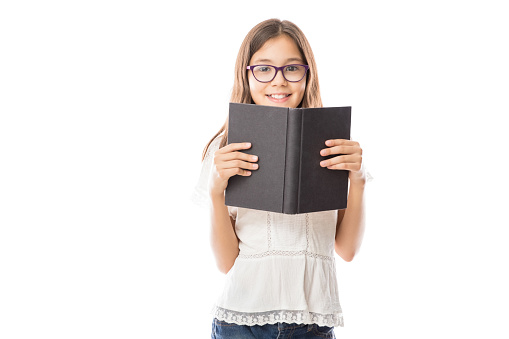 Portrait of little adorable girl wearing white shirt and spectacles holding open book against white background