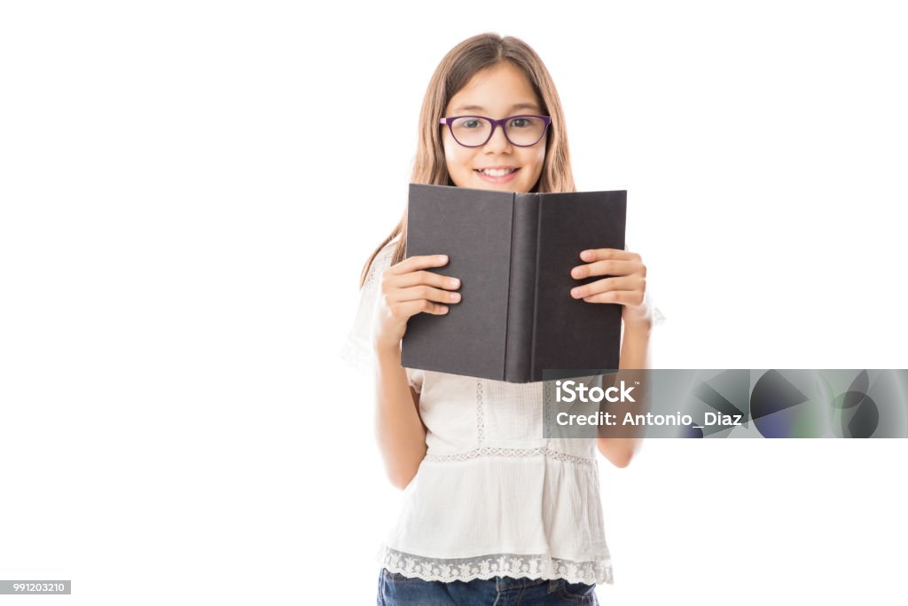 Cheerful girl holding a book looking at camera Portrait of little adorable girl wearing white shirt and spectacles holding open book against white background Child Stock Photo