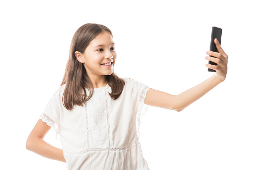 Cute smiling girl in white blouse taking selfie with smartphone isolated on white