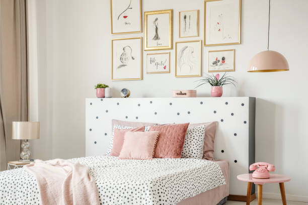 istock Beautiful white bedroom interior with feminine decor, polka dot pattern, pink accessories and framed sketches gallery on the wall 991205256