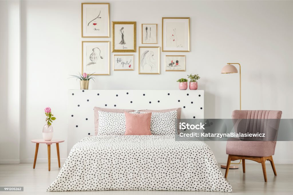 Interni femminili da camera da letto con letto matrimoniale con lenzuola punteggiate, poltrona, collezione d'arte e piante - Foto stock royalty-free di Camera da letto