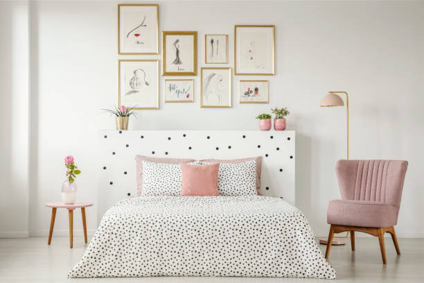 Feminine bedroom interior with a double bed with dotted sheets, armchair, art collection and plants Feminine bedroom interior with a double bed with dotted sheets, armchair, art collection and plants surrounding wall photos stock pictures, royalty-free photos & images