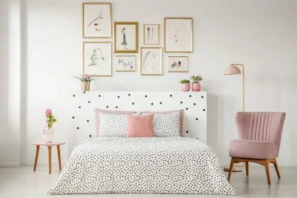 Photo of Feminine bedroom interior with a double bed with dotted sheets, armchair, art collection and plants
