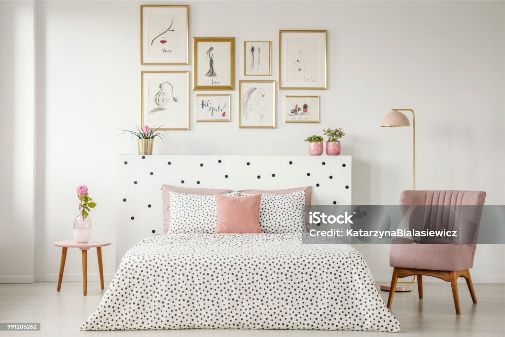 Interior feminina quarto com uma cama de casal com lençóis de pontilhados, poltrona, coleção de arte e plantas - Foto de stock de Quarto de dormir royalty-free