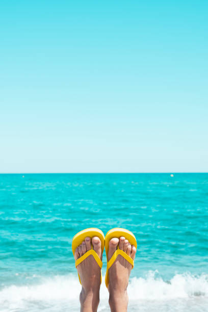 Woman relaxing on a pebble beach with pink water shoes, enjoying the sea view
