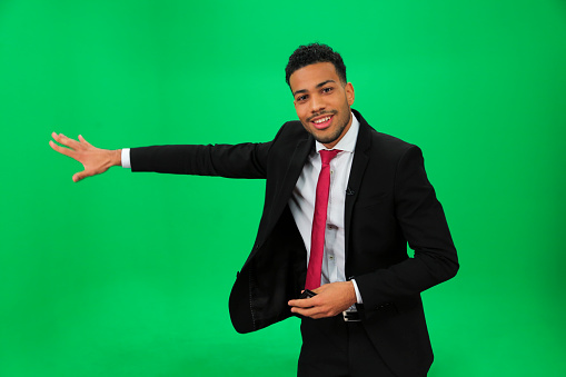 Young afro-american weather man in front of a green background with small remote in his other hand.