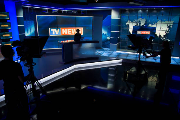 News filming studio TV news studio ready for filming. Tv news anchor sitting in his place and two camera men silhouettes in front of him. stage set stock pictures, royalty-free photos & images