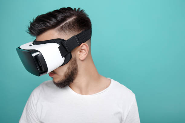 istock Young handsome bearded man looking down with virtual reality goggles in studio on colorful background. Smartphone using with VR headset. 991249194