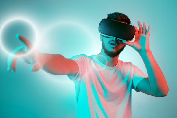 istock Attractive bearded man trying VR headset and poniting. Young man exploring another world with virtual reality goggles on the colorful background. 991249764