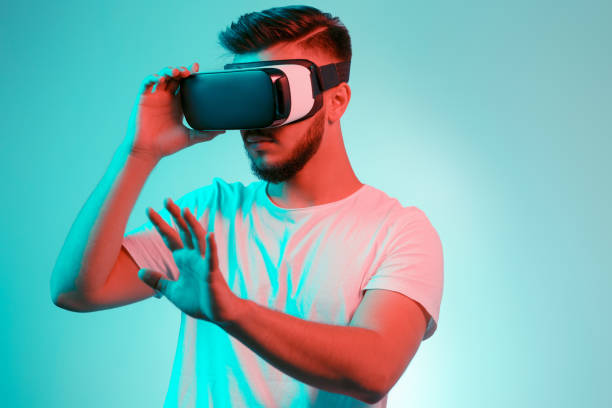 istock Handsome bearded man trying VR headset and exploring another world on the colorful background. Smartphone using with VR headset. 991250084