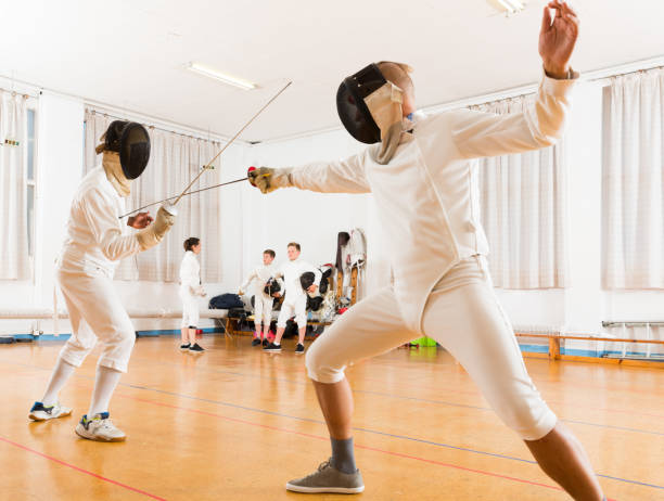 Adults and teens wearing fencing uniform practicing with foil Adults and teens wearing a fencing uniform practicing with foil in the gym fencing sport stock pictures, royalty-free photos & images