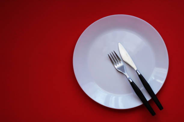 istock White plate, fork and the knife, red background 991279618