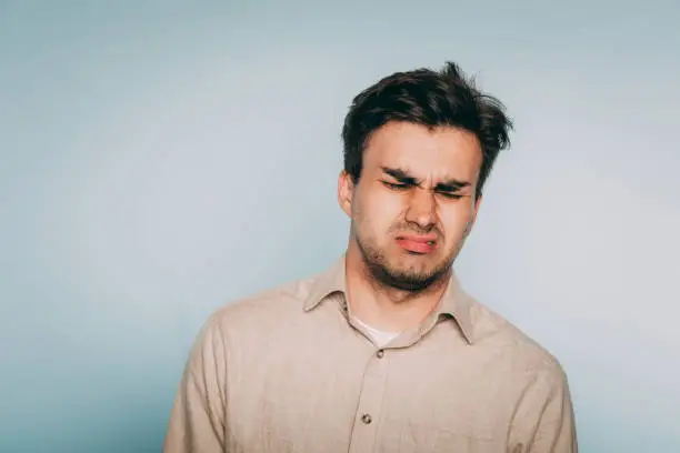 nausea aversion repulsion. reluctant man grimacing in disgust. portrait of a young brunet guy on light background. emotion facial expression. feelings and people reaction concept.