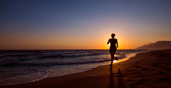 Female runner on a beach at sunset.